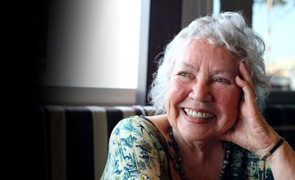 Merle Thornton AM a grey-haired woman smiles resting her head on her hand